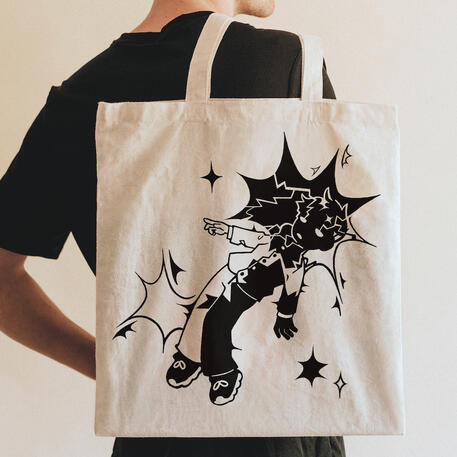 image of a beige tote being held. the design on the bag is of a boy floating with sparkles and star-like shapes near his head and legs. there is a mix between parts of the boy and stars that are colored in black while some parts are left uncolored to show