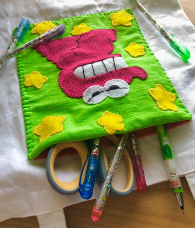 a different angle of the tote laid on a table. there are pens, pencils, and a pair of scissors coming out of the chocobi pocket.